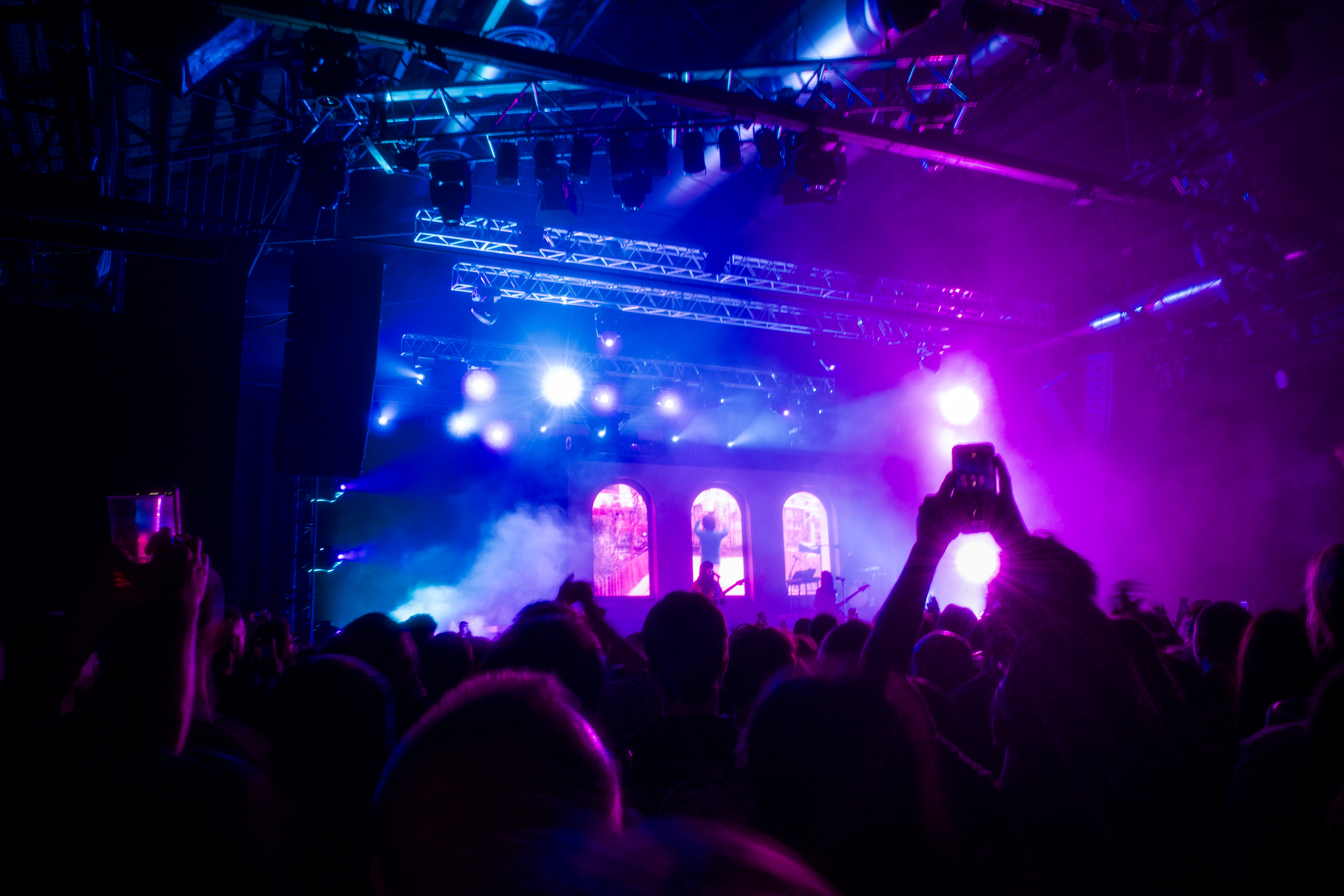 Khruangbin performing on stage, purple and blue lighting, view from crowd